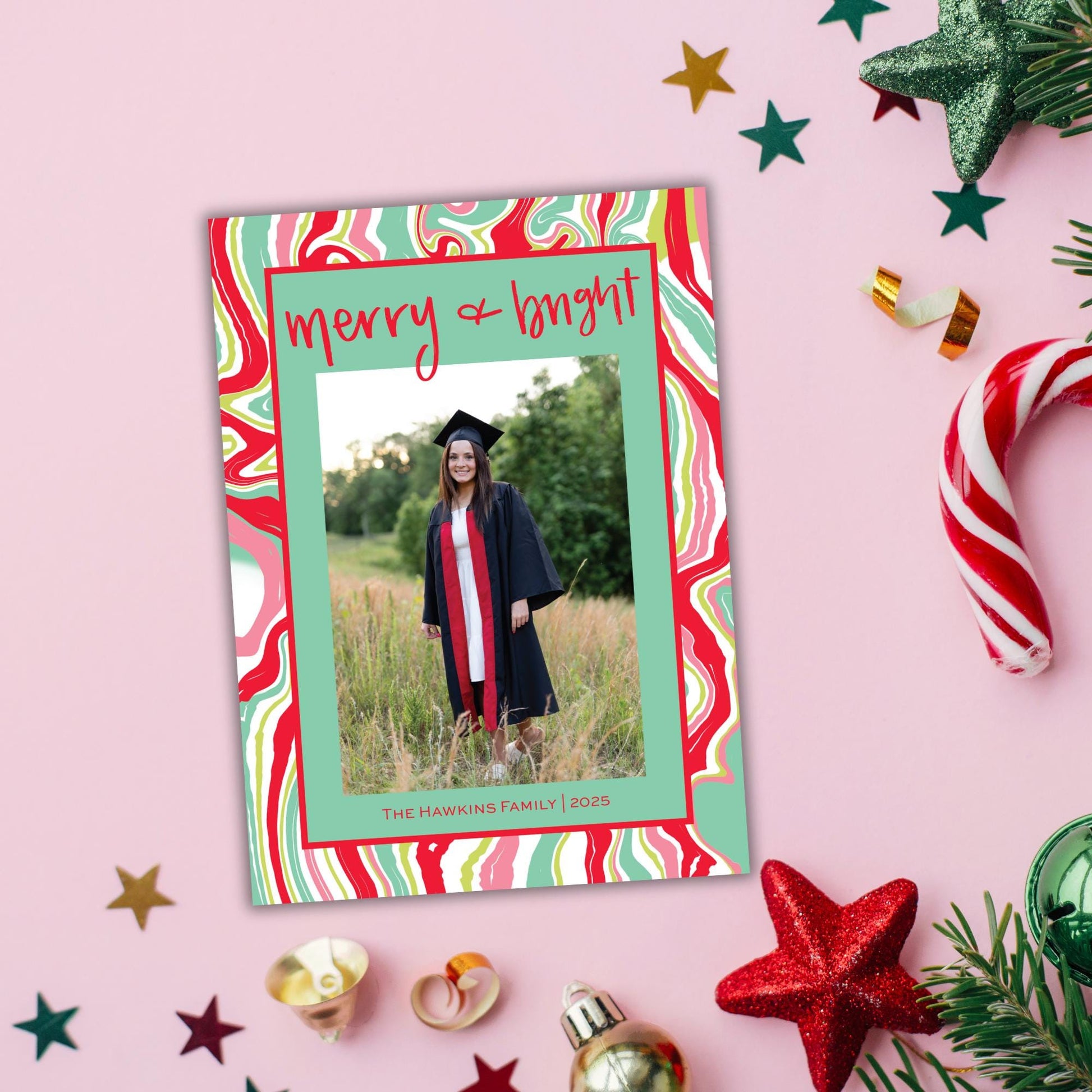 a colorful graduation card with a photo of a smiling woman in a graduation gown, surrounded by festive decorations such as candy canes, star ornaments, and pine branches.