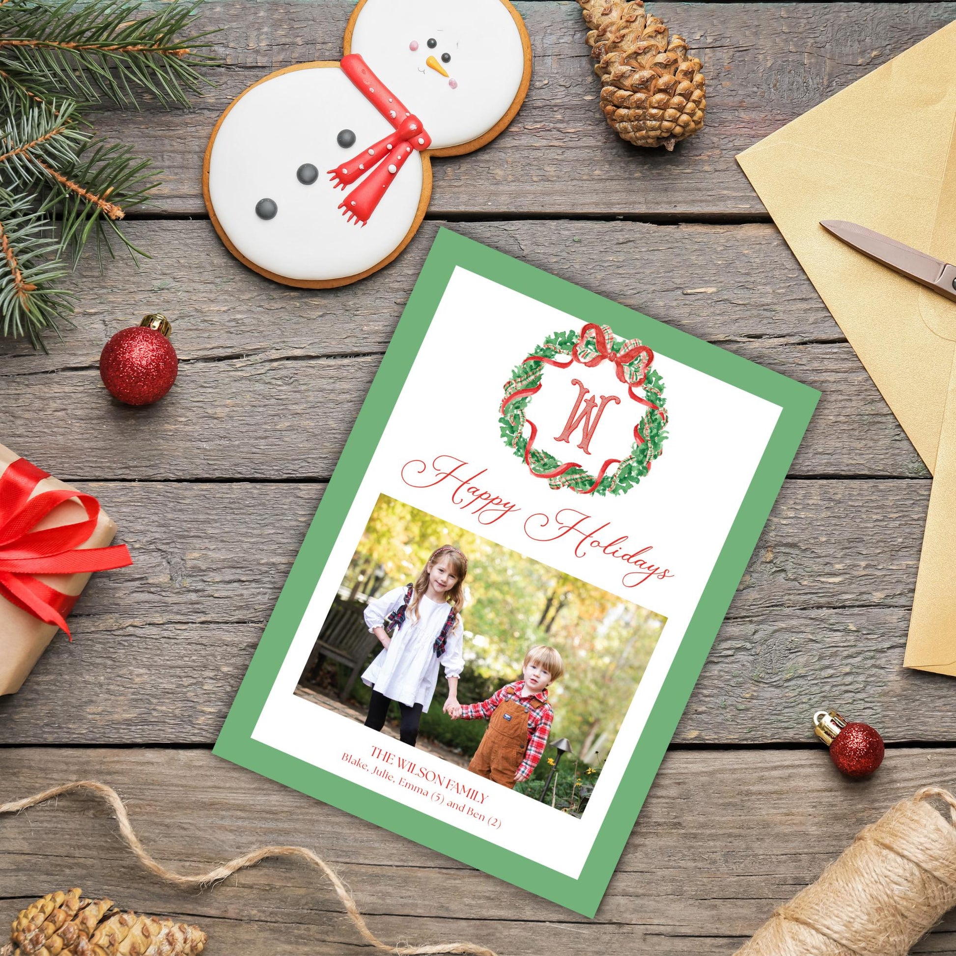 A green and white holiday greeting card with a photo of two children, surrounded by Christmas decorations such as a snowman, pine cones, and ornaments.