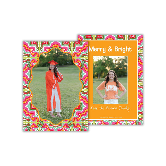 A colorful greeting card featuring a young woman in an orange graduation gown standing in a grassy field.