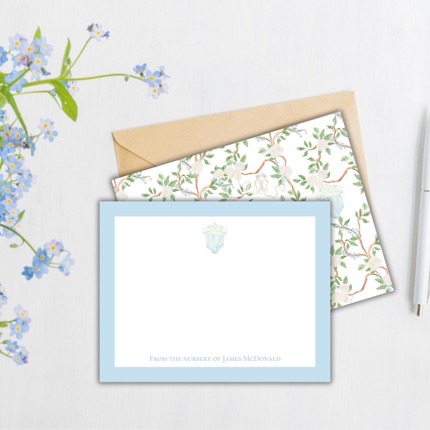 a blue and white stationery set with a floral pattern, placed on a white surface next to a pen and a flower arrangement.