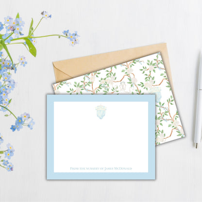 a blue and white stationery set with a floral pattern, placed on a white surface next to a pen and a flower arrangement.