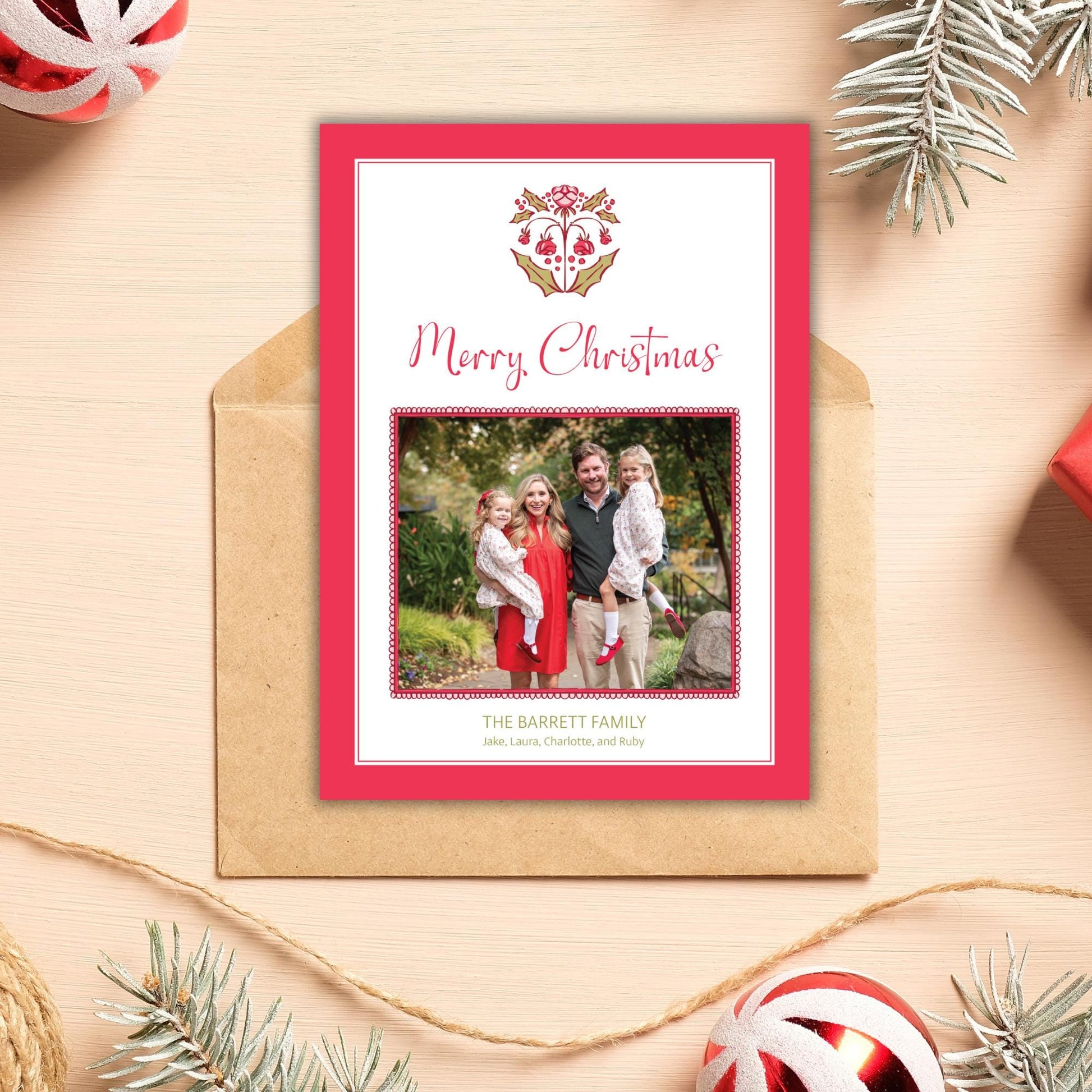 A Christmas card with a family photo and the text &quot;Merry Christmas&quot; is displayed on a wooden surface, surrounded by Christmas decorations such as ornaments and pine branches.