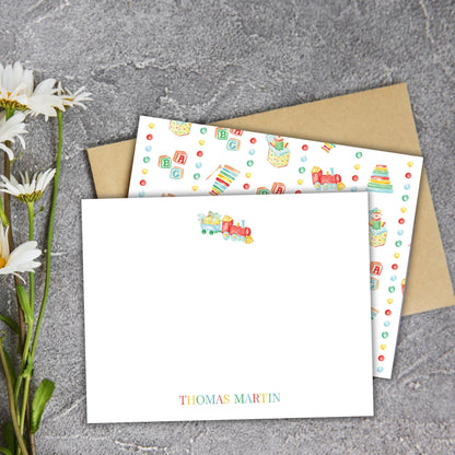 a white card with a train design and a blank card with a colorful pattern on a gray surface.