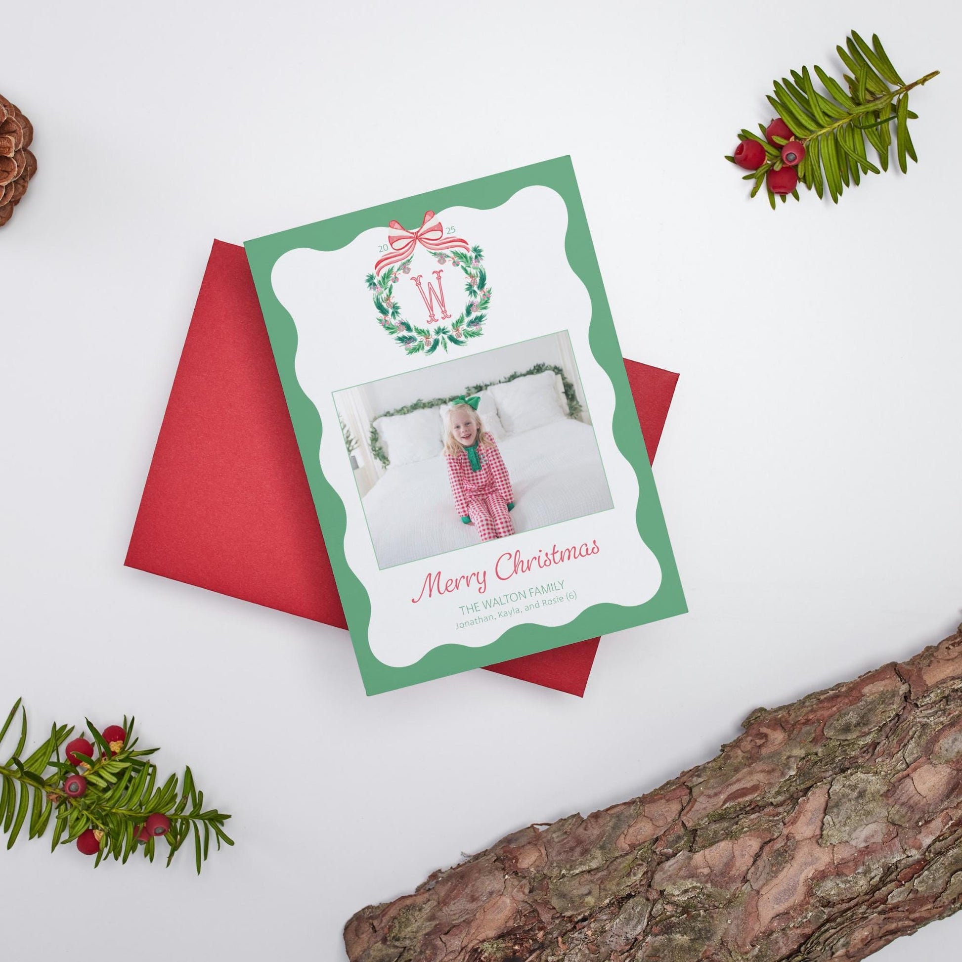 A Christmas card with a photo of a young girl in a pink outfit, surrounded by holiday decorations such as a wreath, pine branches, and red envelopes.