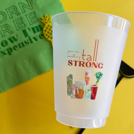 A white plastic cup with a colorful design featuring various drinks, along with the text "pour me something tall & strong".