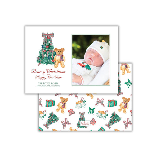 The image is a Christmas card featuring a baby wearing a white outfit and a teddy bear, with a Christmas tree and other holiday-themed illustrations.
