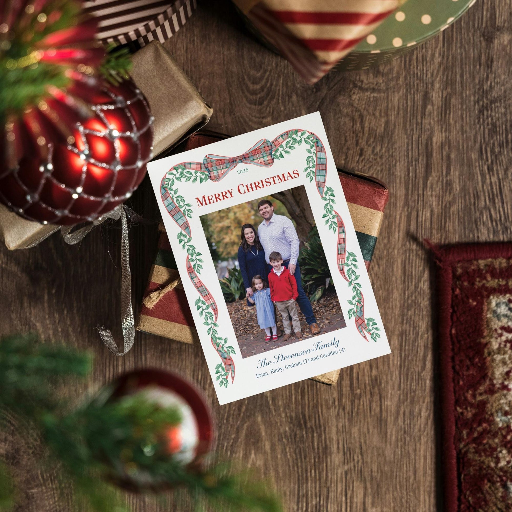 A Christmas card with a family photo is placed on a wooden surface, surrounded by wrapped gifts and ornaments.