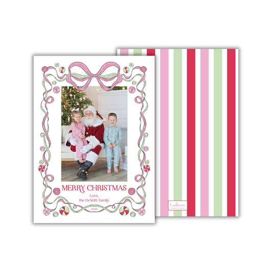 A Christmas card featuring a Santa Claus figure, with a family photo in the center. The card has a decorative border with pink and green stripes.