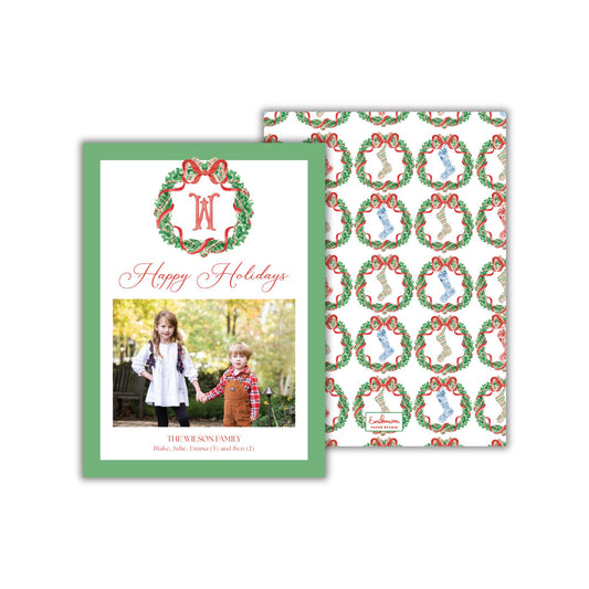 A green and white holiday card with a photo of two children, one girl and one boy, standing together in front of a wreath. The card has a repeating pattern of Christmas wreaths on the background.