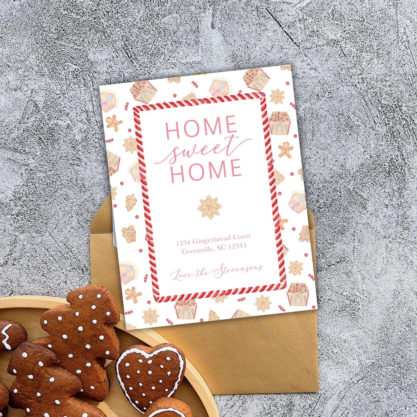 a card with a festive design, including a pattern of gingerbread houses and other holiday-themed elements, placed on a wooden surface next to a plate of gingerbread cookies.