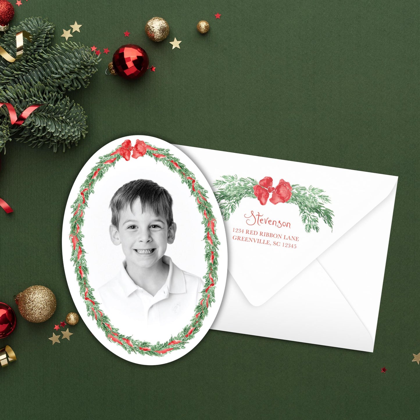 A framed black and white photograph of a young boy is displayed next to an envelope with a holiday-themed design, surrounded by Christmas ornaments and a green background.