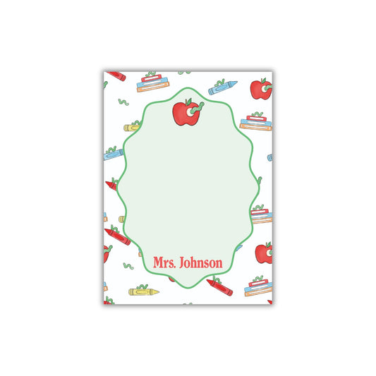 The image is a personalized nameplate with a repeating pattern of apples, crayons, and books. The nameplate has a green border and the name "Mrs. Johnson" written on it.