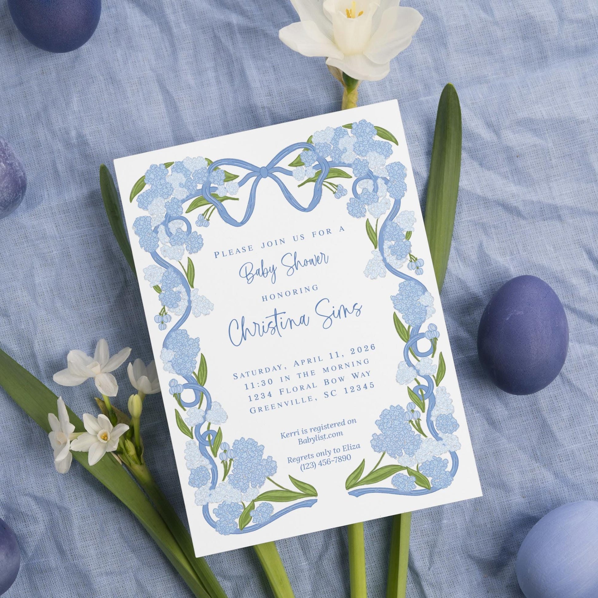 The image is a baby shower invitation featuring blue flowers and Easter eggs, with a blue and white color scheme.